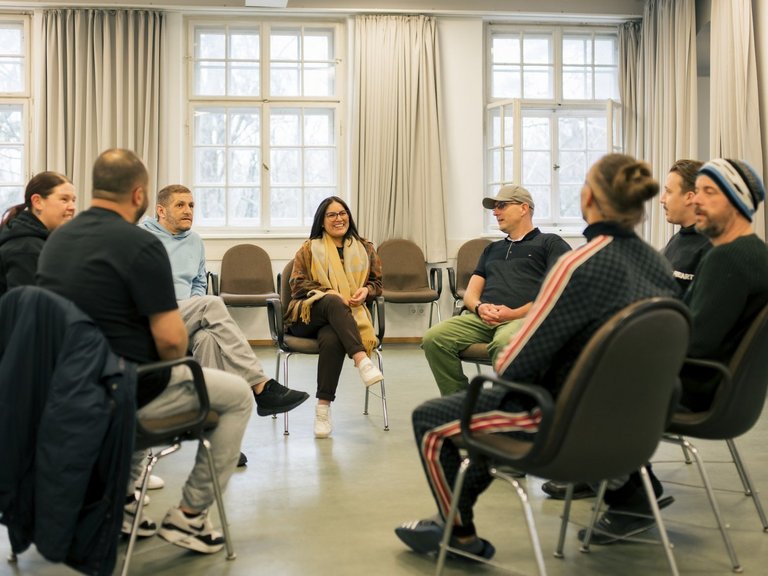 Acht Menschen sitzen in einem Stuhlkreis und unterhalten sich.